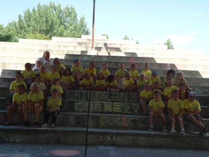 Children's Corner summer camp group on amphitheater steps beside their name written in chalk